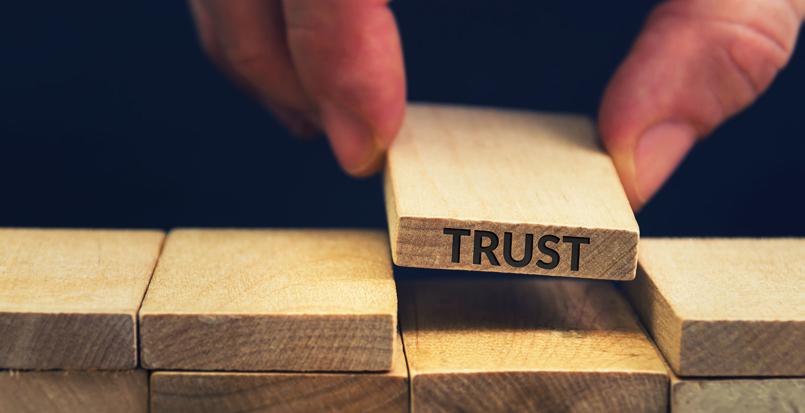 image of someone picking up wooden block with the word "trust" written on the side